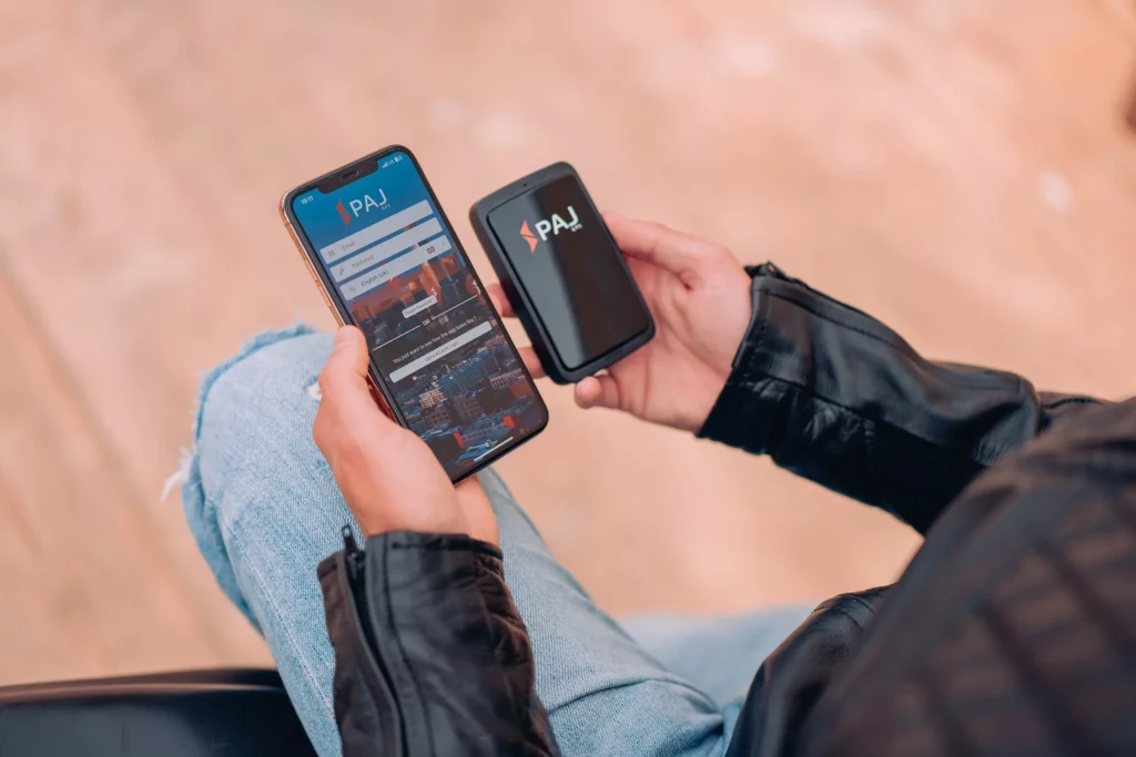 Mini GPS tracker in one hand and PAJ finder portal opened in his mobile