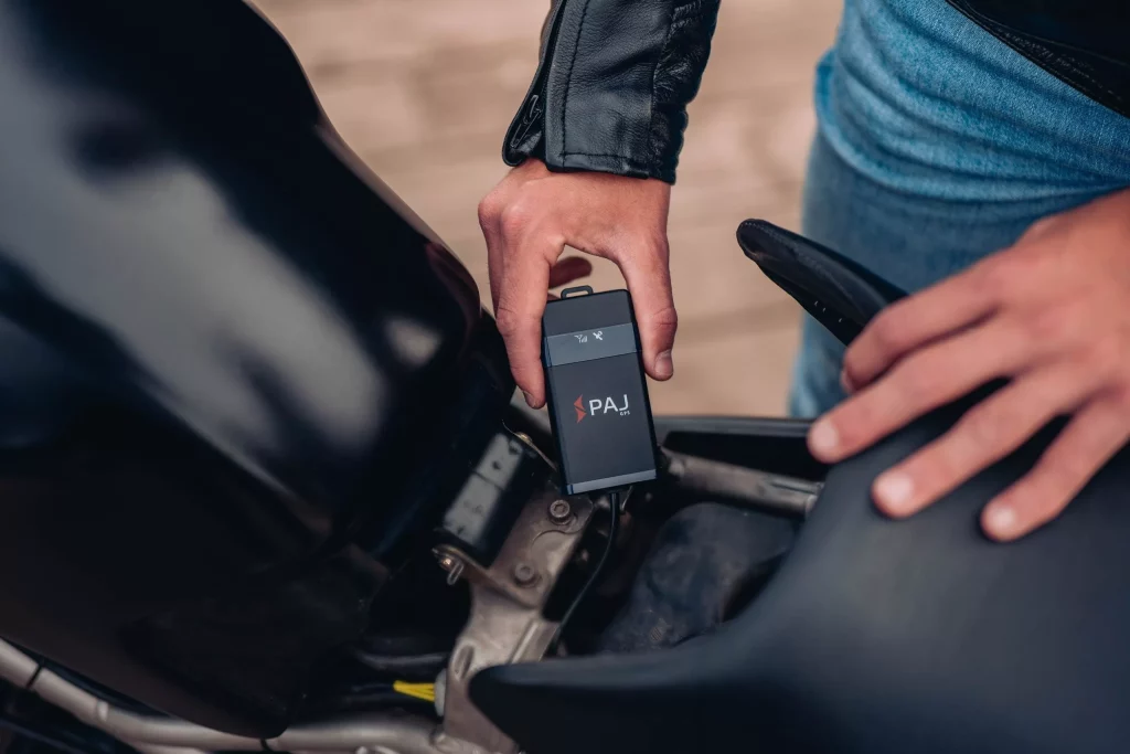 man standing beside the motorcycle holding GPS tracker for motorcycles
