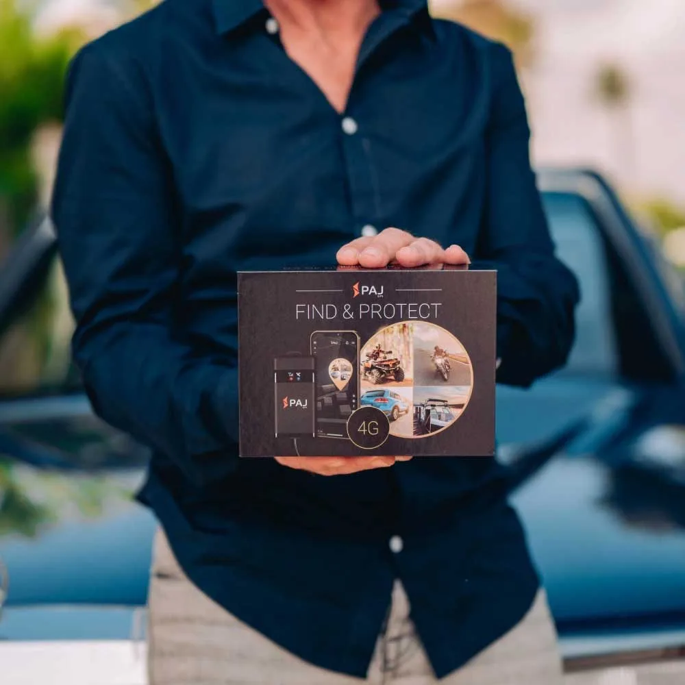 A man in blue shirt infront of his black car holding vehicle finder 4g gps tracker box. it is a vehicle tracker device